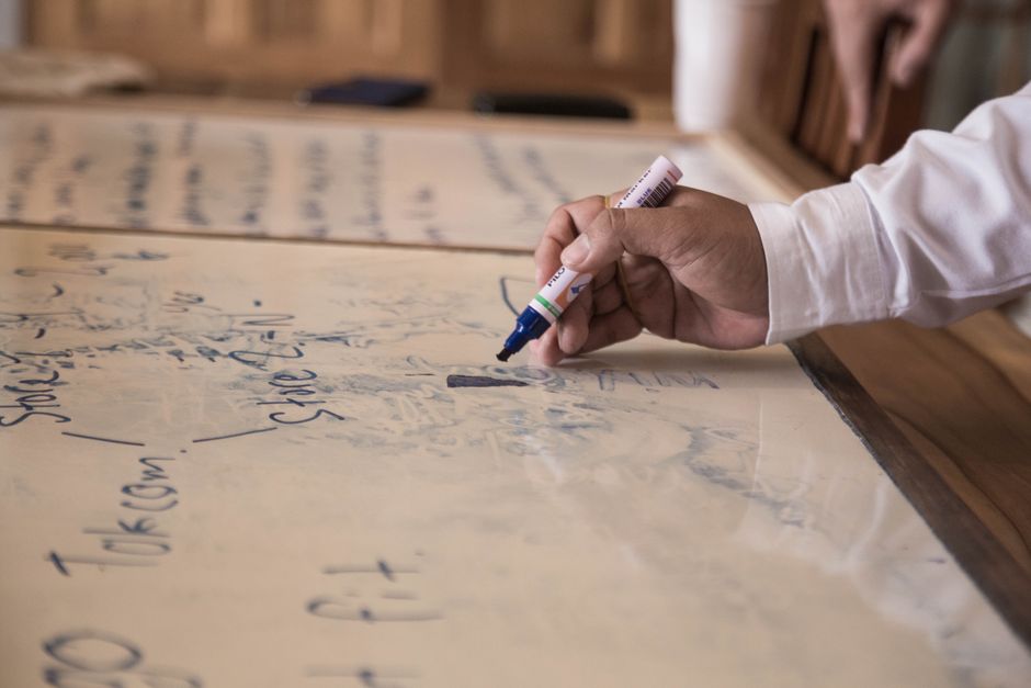 Focused view of a hand using a marker to write on a whiteboard in an indoor office setting.