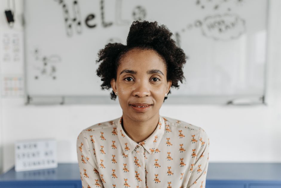 A confident woman with afro hair poses in a classroom, fostering an educational theme.