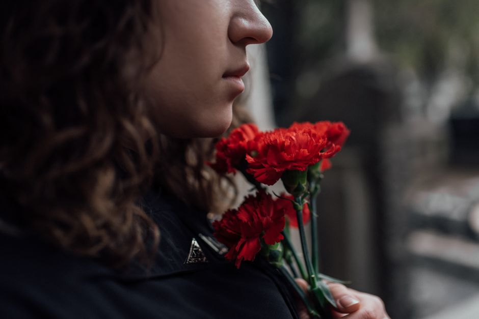 Side profile of a woman holding red carnations, symbolizing grief and loss.